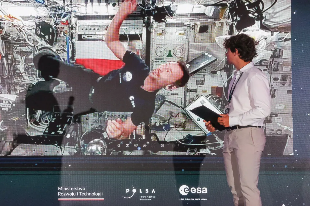 Łódź, 02.07.2025. Przebywający na Międzynarodowej Stacji Kosmicznej polski astronauta Sławosz Uznański-Wiśniewski (na ekranie) podczas połączenia wideo na żywo w EC1 w Łodzi, 2 bm. Podczas trwającego ok. 20 minut połączenia Sławosz Uznański-Wiśniewski wykonywał eksperymenty w stanie nieważkości oraz odpowiadał na pytania zadawane przez młodzież. (jm) PAP/Marian Zubrzycki
