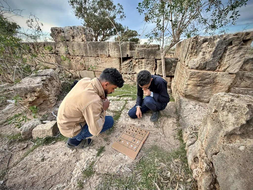 Mieszkańcy Tolmeity, Ismail i Hasan, pokazują różne warianty gry siza na wykonanej własnoręcznie kartonowej planszy  (fot. Zofia Kowarska)