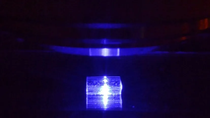 Pobudzany światłem niebieskim kryształ fluorku litu z zarejestrowanymi śladami cząstek jonizujących podczas obserwacji pod mikroskopem fluorescencyjnym. (Źródło: IFJ PAN)